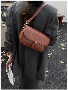 Close-up of retro brown saddle bag showing matte leather texture and gold buckle detail