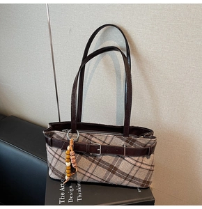Detail of vintage plaid baguette bag featuring leather buckle and ethnic beaded charm