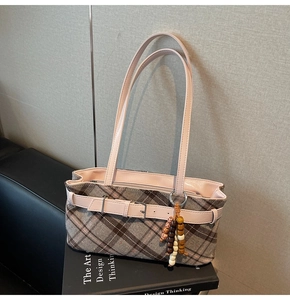 Detail of plaid shoulder bag with pink leather strap and vintage beaded charm on a book