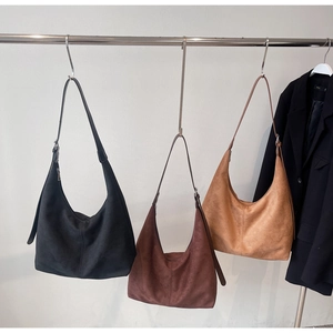Three minimalist matte suede tote bags in black, dark brown, and caramel on metal hooks