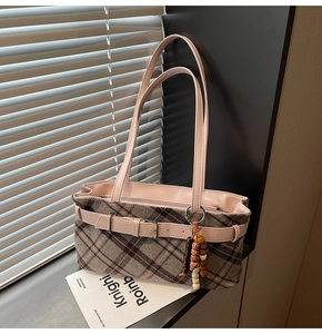 Detail of tweed checkered shoulder bag featuring pink leather trim and retro charm pendant