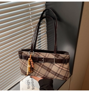 Detail of plaid tote bag featuring leather straps and colorful beaded wooden charm