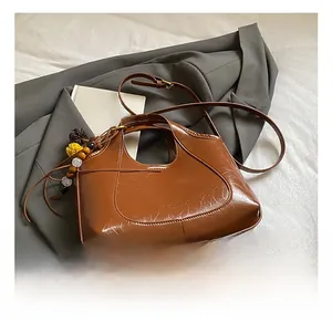 Détail d'un sac seau en cuir caramel avec pompon décoratif et pendentif en perles
