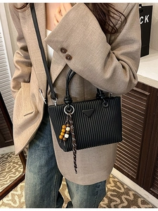 Sac seau plissé noir chic avec logo en métal et pompon perlé porté par un mannequin