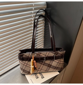 Detail of plaid tweed shoulder bag with dark brown patent leather strap and beaded charm