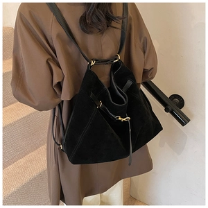 Detail of black suede tote bag with gold hardware and drawstring on indoor staircase