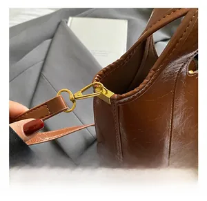 Détail du crochet en métal doré et de la texture en similicuir marron ciré du sac