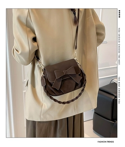 Detail of dark brown saddle bag with large bow decoration and woven handle
