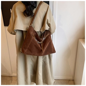 Detail of dark brown suede tote bag with golden metal buckles on a long beige coat