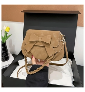 Brown bow shoulder bag in a black gift box with tulips and books in the background