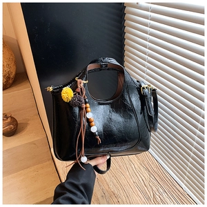 Détail d'un sac demi-lune en cuir ciré noir avec pompon décoratif et bandoulière fine