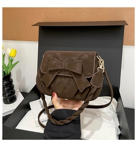 Detailed close-up of dark brown suede handbag with large bow and woven strap in gift box