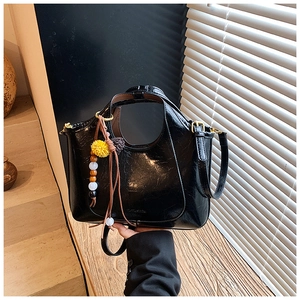 Détail d'un sac à main noir brillant avec poignée ronde et pendentif en peluche coloré