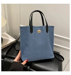 Detail of blue denim bucket bag with black leather straps and gold metal twist-lock closure