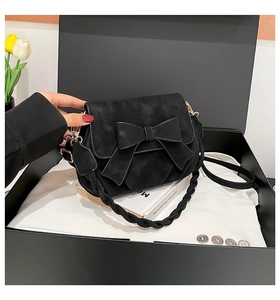 Detail of black suede shoulder bag with a large bow in a luxury gift box setting