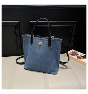 Close-up of blue denim tote bag featuring a gold metal twist lock and black leather handles
