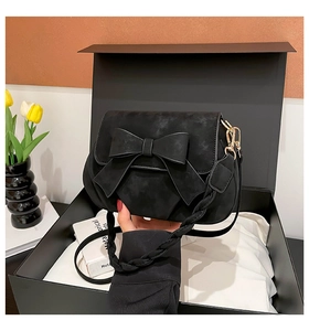 Detail of black suede bag with large bow decoration and woven shoulder strap in gift box