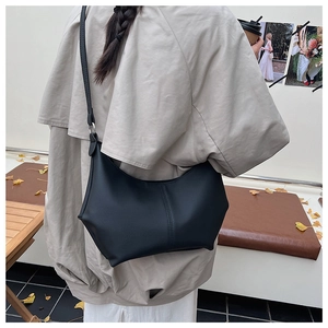 Détail du sac croissant noir minimaliste à bord ondulé porté à l'épaule par un modèle