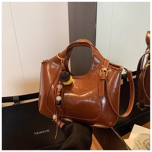 Gros plan du sac cabas marron vintage avec texture cirée brillante et breloque pompon