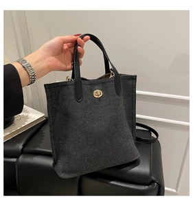 Detail of grey denim tote bag with black leather handle and golden metal turn-lock closure
