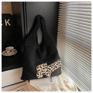Detail of black plush tote bag with leopard print letter M in a cozy setting