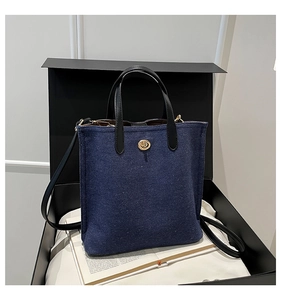 Close-up of a blue denim tote bag with leather handles and gold turn-lock in a gift box
