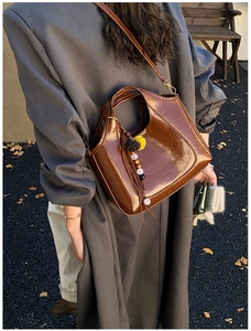 Détail d'un sac seau en daim marron foncé avec pompon coloré dans un décor extérieur