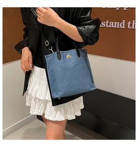 Detail of blue denim tote bag with black leather straps and golden twist lock closure
