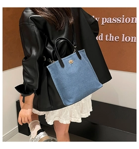 Detail of blue denim bucket bag with black leather handle and golden metallic buckle