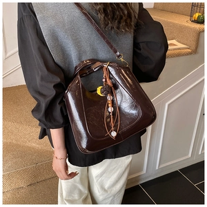 Détail du sac seau marron foncé brillant avec breloque perlée et bandoulière fine