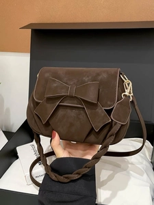 Vintage dark brown crossbody bag featuring a large bow and woven strap on a gift box