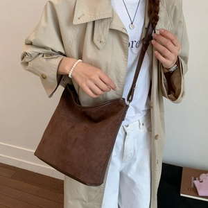 Detail of dark brown frosted leather bucket bag with fine stitching on model in beige coat