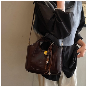 Détail du sac à bandoulière en cuir ciré marron foncé avec un pendentif à pompons colorés