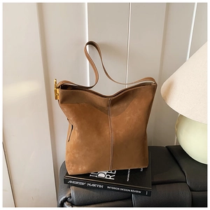 Macro view of textured brown suede tote bag featuring white stitching and gold buckles