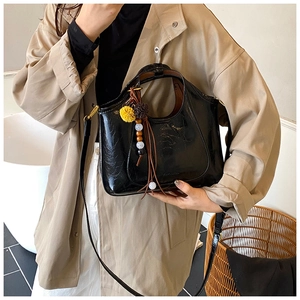 Détail du sac bandoulière noir brillant avec pompons et perles sur un trench-coat beige