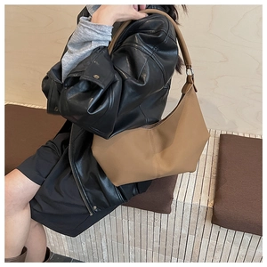 Gros plan du sac hobo en cuir mat kaki porté à l'épaule avec une veste en cuir noir stylée
