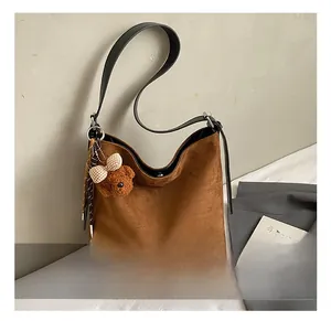 Detail of brown suede bucket bag featuring a cute plush bear charm with a plaid bow