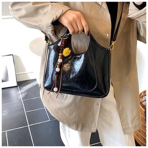 Détail du sac hobo noir brillant avec breloque à pompon ethnique et texture froissée