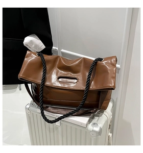 Detail of a brown PU leather tote bag with thick woven rope straps on a white suitcase