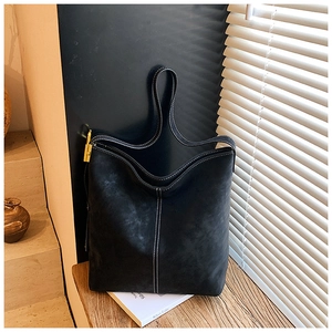 Detail of matte black bucket bag showing white contrast stitching and gold metal lock