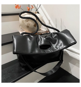 Detail of glossy black leather tote bag with thick braided rope handle on stairs