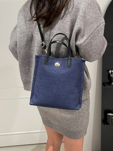 Blue denim tote bag with black leather handles and gold lock worn by a model