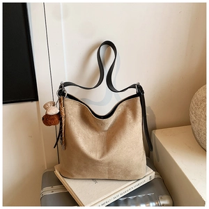 Detail view of khaki suede tote bag with brown plush bear charm on white book