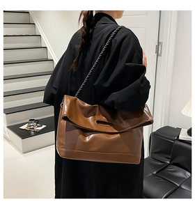 Detail of a large brown tote bag with a unique fold-over flap and black woven rope strap