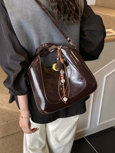 Sac seau en cuir marron foncé brillant avec breloques rétro porté à l'épaule