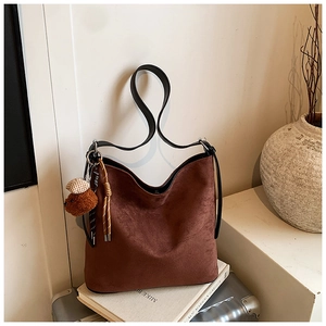 Detail of dark brown matte tote bag featuring plush bear charm and woven cord detail