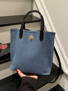 Blue denim tote bag with black leather handles and gold clasp in hand-held pose