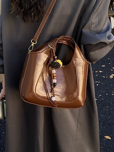 Sac à bandoulière marron plissé brillant avec breloque bohème présenté en décor extérieur