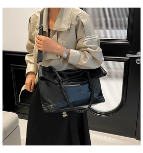 Detail of black large tote bag with woven handles and wide nylon shoulder strap on model