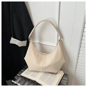 Détail d'un sac hobo beige posé sur une valise argentée à côté d'un magazine ouvert